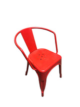 Red metal chair in a warehouse setting with cardboard boxes and equipment in the background.