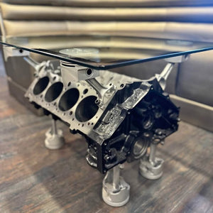 Engine block used as a glass-top table on a wooden floor.