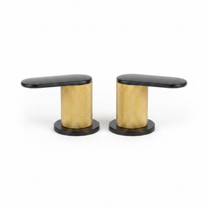 Two modern kitchen faucet handles with black tops and bases and a textured gold mesh center, shown on a speckled kitchen countertop with a blurred kitchen background.