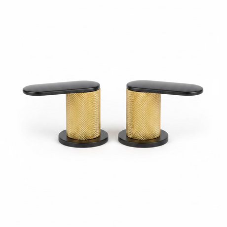 Two modern kitchen faucet handles with black tops and bases and a textured gold mesh center, shown on a speckled kitchen countertop with a blurred kitchen background.