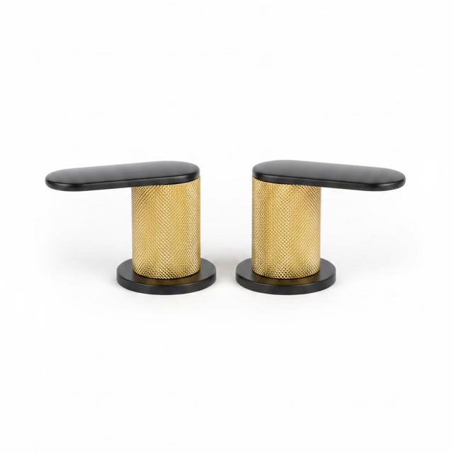 Two modern kitchen faucet handles with black tops and bases and a textured gold mesh center, shown on a speckled kitchen countertop with a blurred kitchen background.