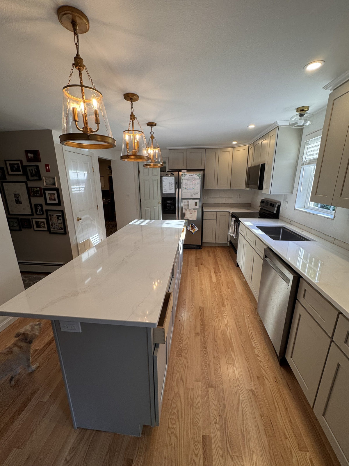 After: long Viatera quartz island beside KCD Shaker Sand cabinets and hardwood floors in Goffstown, NH