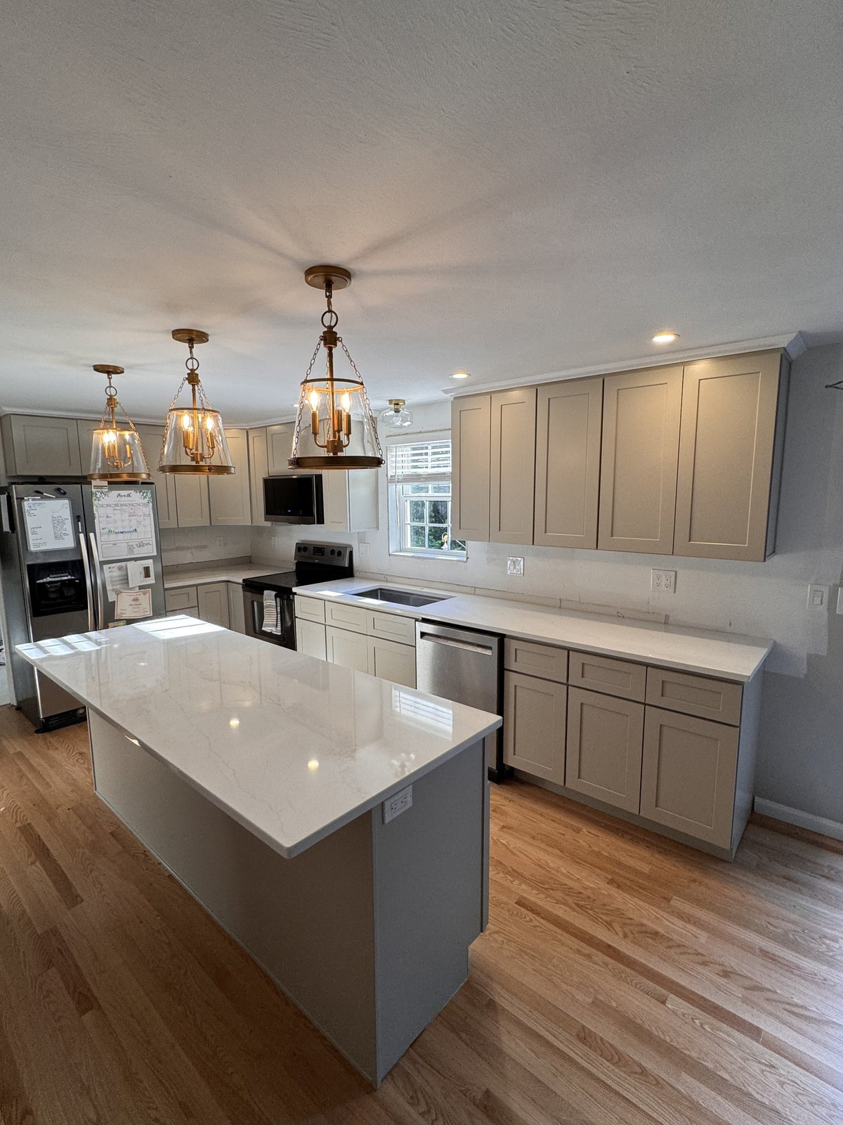 After: Goffstown kitchen with KCD Shaker Sand cabinetry, quartz island and three brass pendant lights