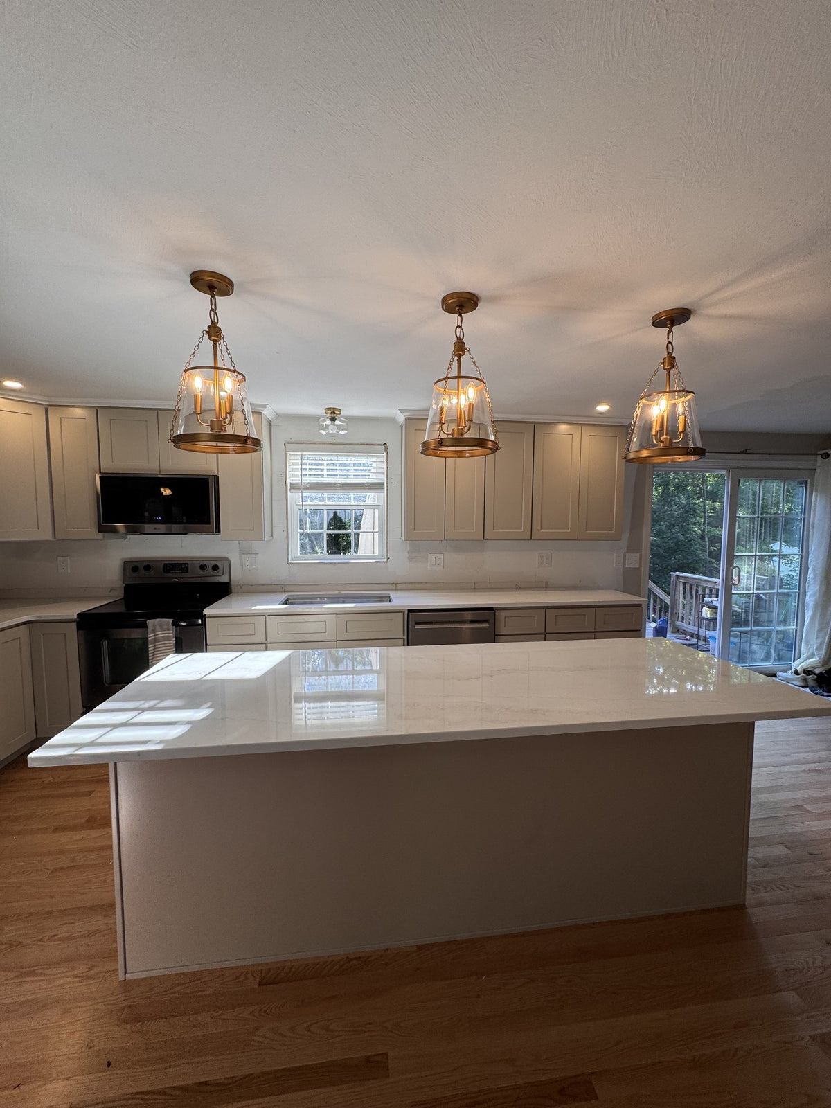 After: large Viatera quartz island under three pendant lights facing the KCD Shaker Sand cabinet wall