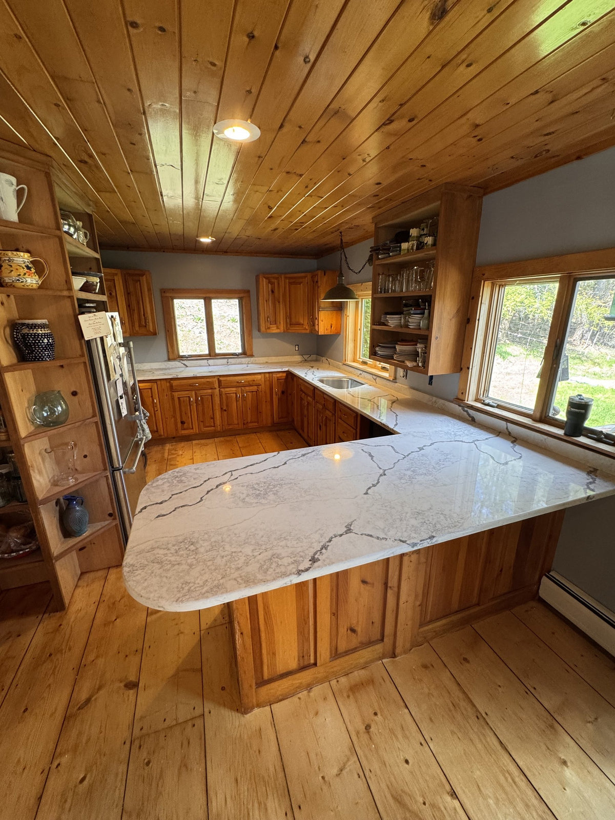 After: Viatera quartz with gray veining across the Vermont cottage kitchen and rounded peninsula