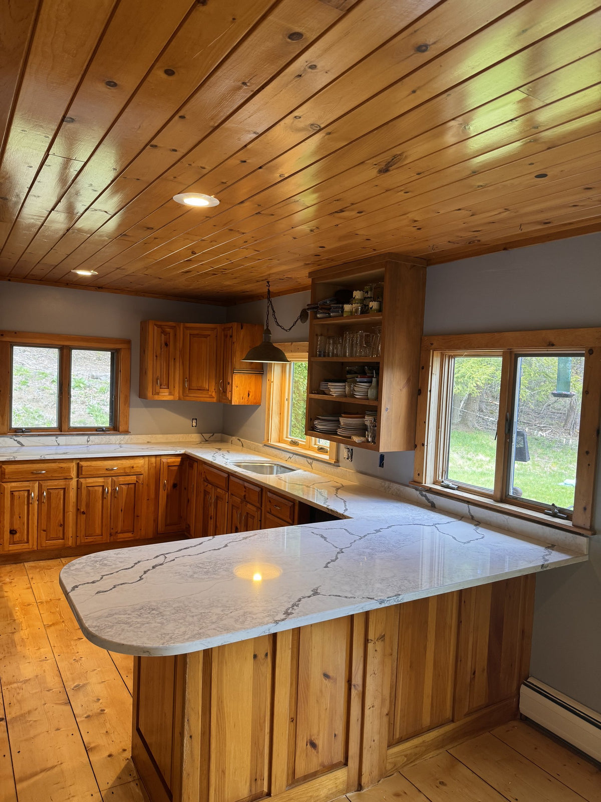 After: rounded Viatera quartz peninsula against knotty-pine cabinetry in a Vermont cottage